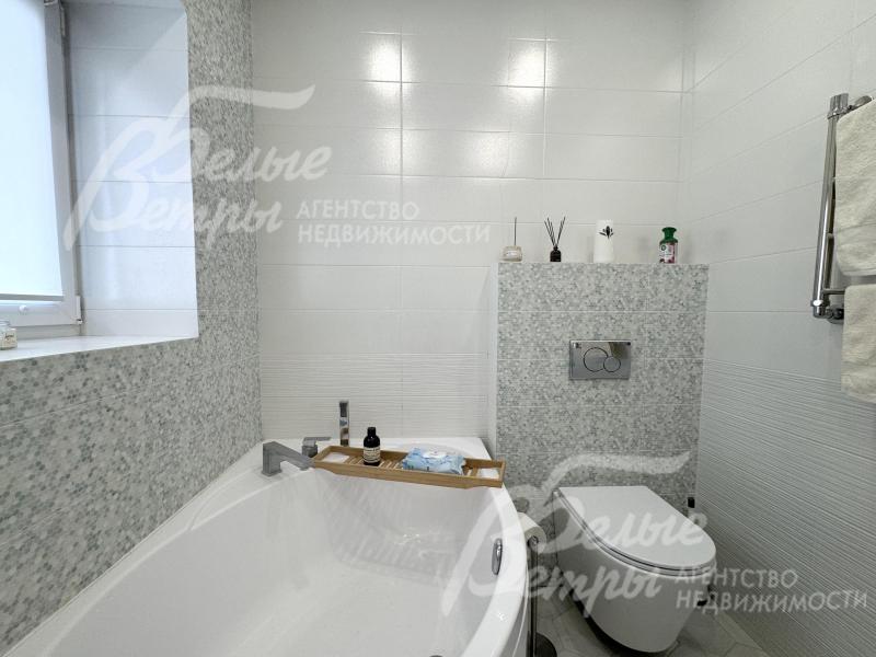 Большая часть стен санузла отделана крупной белой плиткой , акцентные стены оформлены плиткой с нежным серо-белым узором