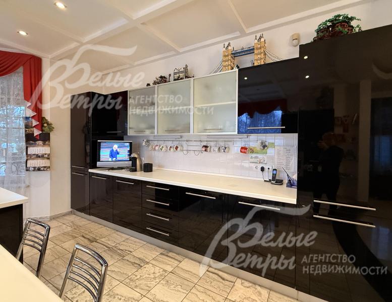 На кухне установлен гарнитур с контрастным сочетанием глянцевых фасадов глубокого чёрного цвета и светлых элементов