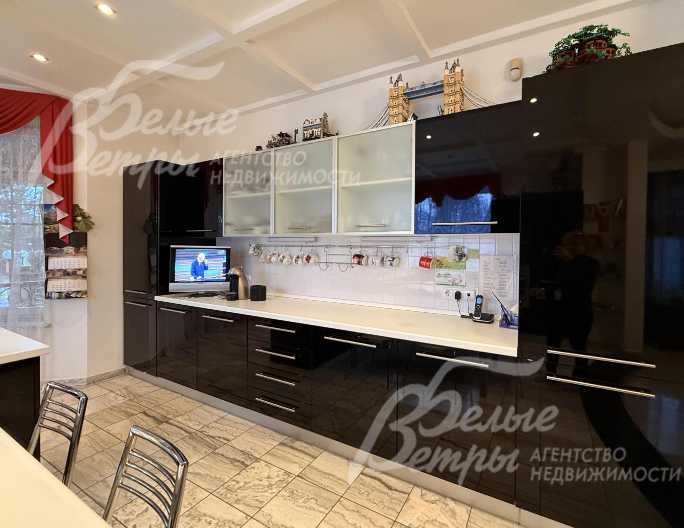 На кухне установлен гарнитур с контрастным сочетанием глянцевых фасадов глубокого чёрного цвета и светлых элементов