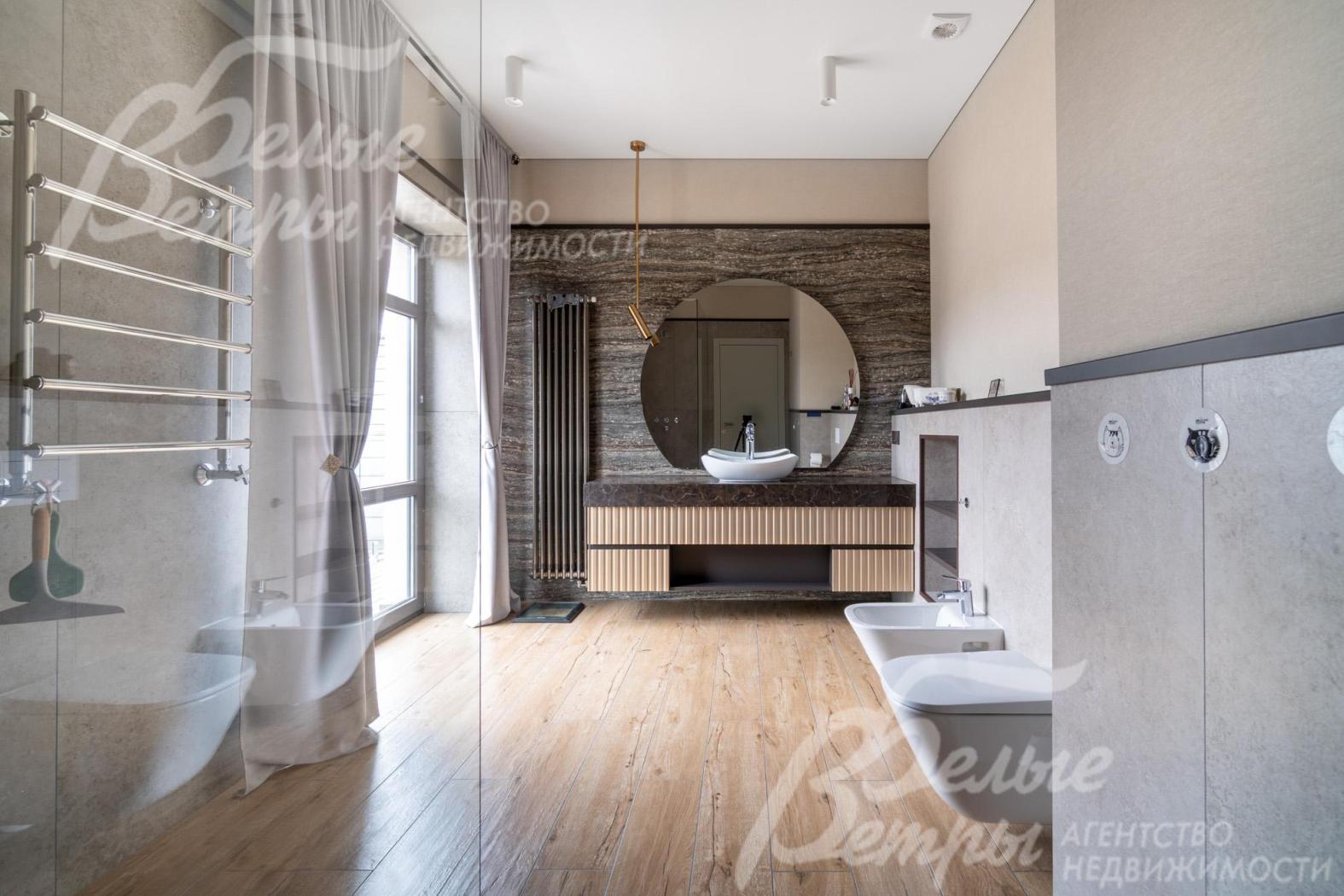 Просторный санузел - с большим окном в пол и душевой со стеклянной перегородкой. Акцентная деталь — большое круглое зеркало над накладной раковиной на подвесной тумбе