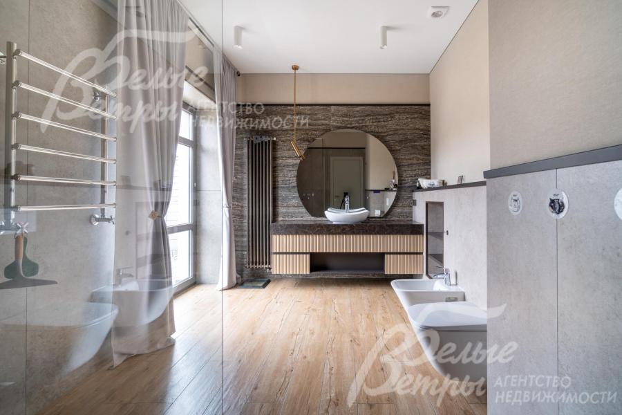 Просторный санузел - с большим окном в пол и душевой со стеклянной перегородкой. Акцентная деталь — большое круглое зеркало над накладной раковиной на подвесной тумбе