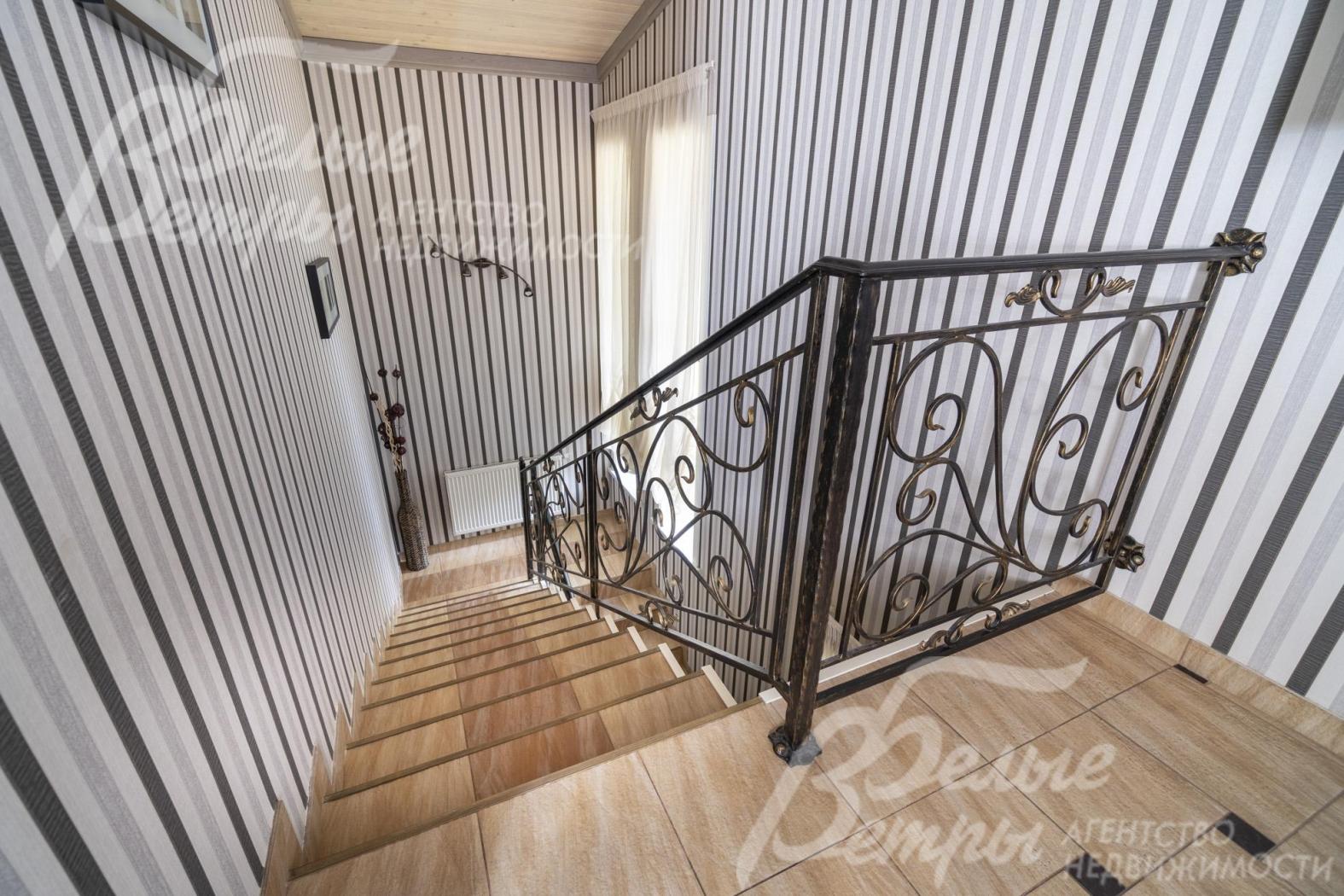 На второй этаж гостевого дома ведёт лестница, отделанная керамогранитом, с коваными перилами