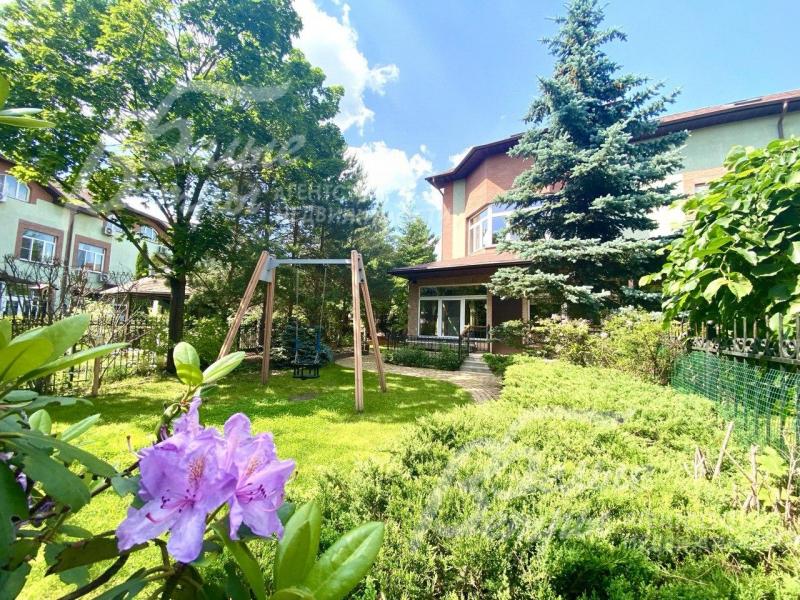 На участке взрослые деревья и декоративные кустарники и цветники.