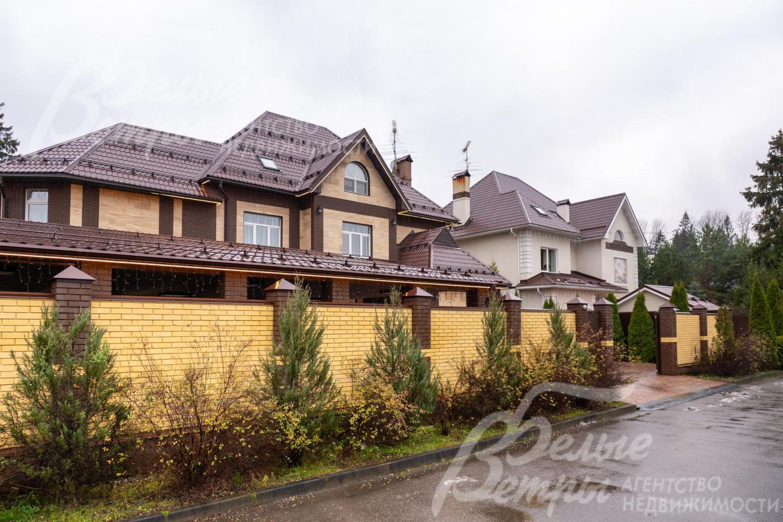 По фасадной части участок огорожен кирпичным забором с декоративными столбами в стиле дома