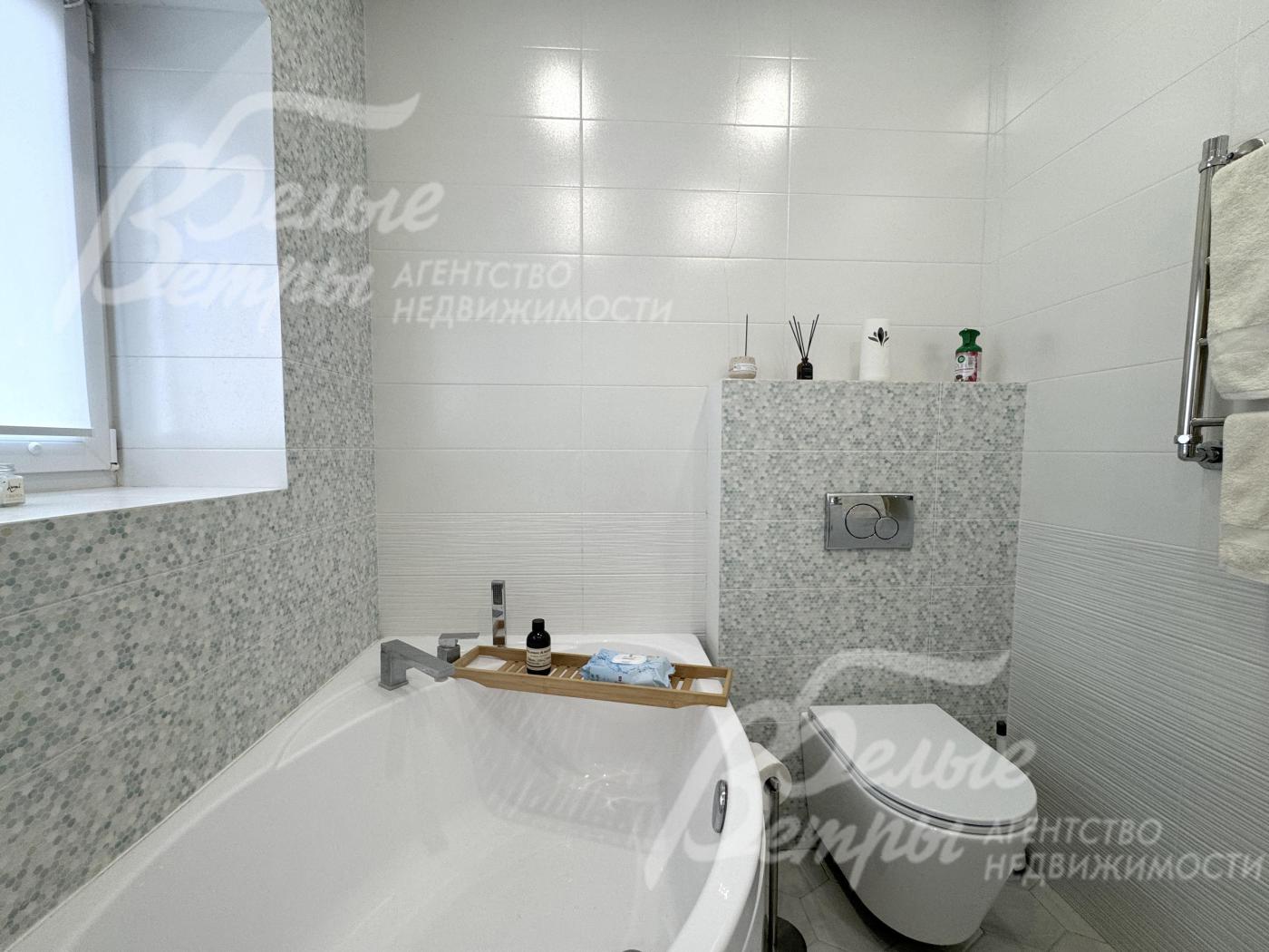 Большая часть стен санузла отделана крупной белой плиткой , акцентные стены оформлены плиткой с нежным серо-белым узором