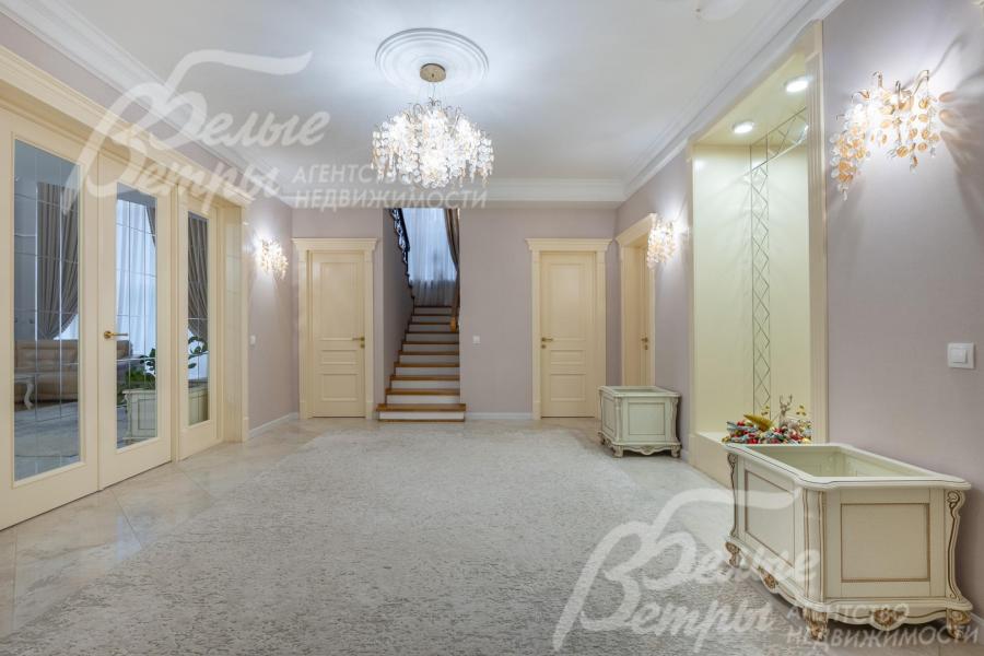 В просторном холле дома уложен уложен керамогранит (тёплый пол), ковёр, интерьер дополняют эксклюзивные скамьи-тумбы, большое зеркало и дорогостоящая люстра